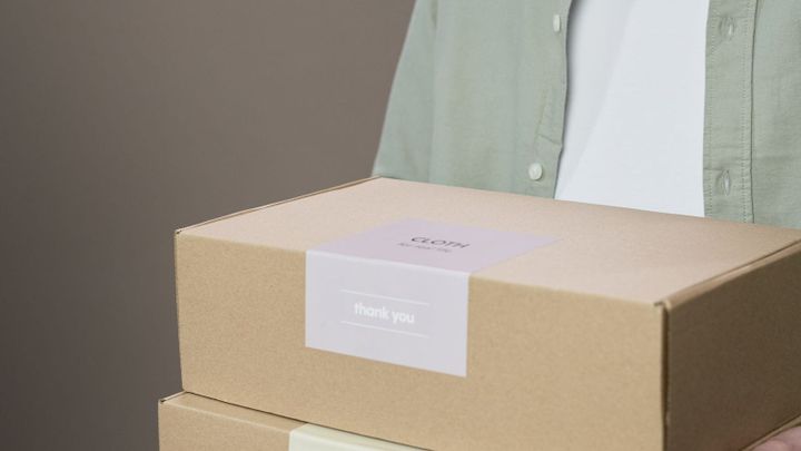 A person carries two cardboard boxes with visible labels on the front.