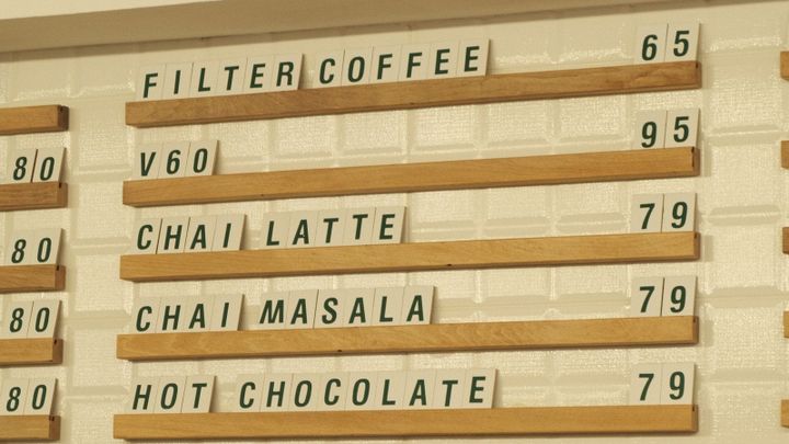 A cafe wall menu lists drink options and prices above a counter.
