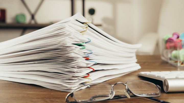 A stack of paper-clipped documents beside eyeglasses and a pen.