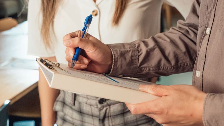 A person writes on a clipboard with a pen.