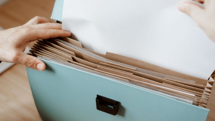 Hands sort papers in a file box with tabbed folders.