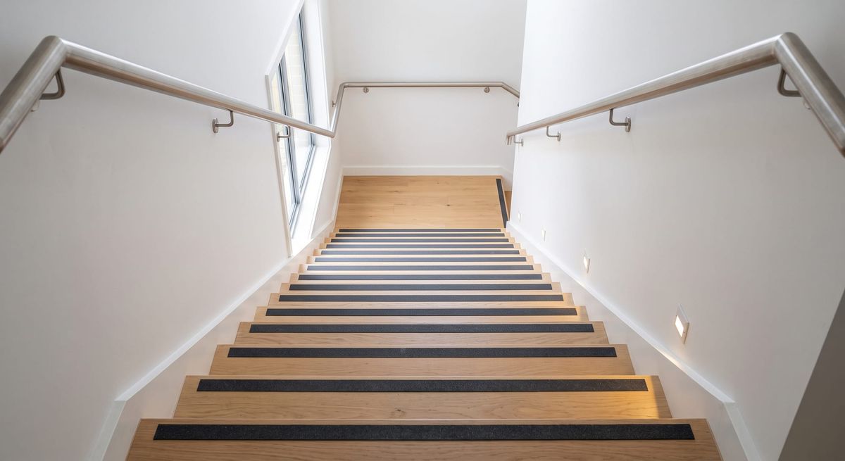 A well-lit indoor staircase featuring strong light-dark contrast on the edge of each step and continuous handrails on both sides.