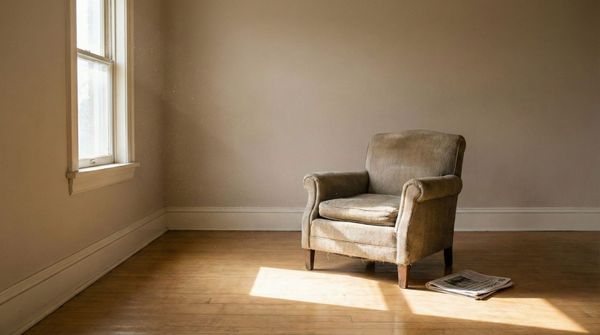 An empty room with scattered papers, a single chair, afternoon light through glass windows, no furniture.
