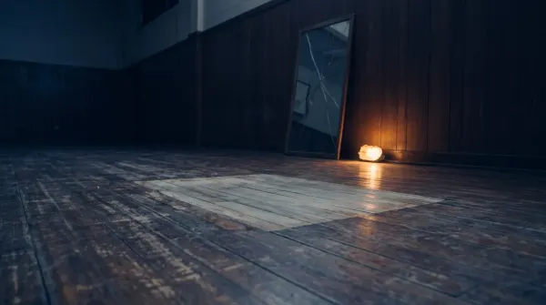 A worn patch on a wooden gym floor where the same stance has been practiced for years, facing a cracked mirror, lit by a single low warm glow.