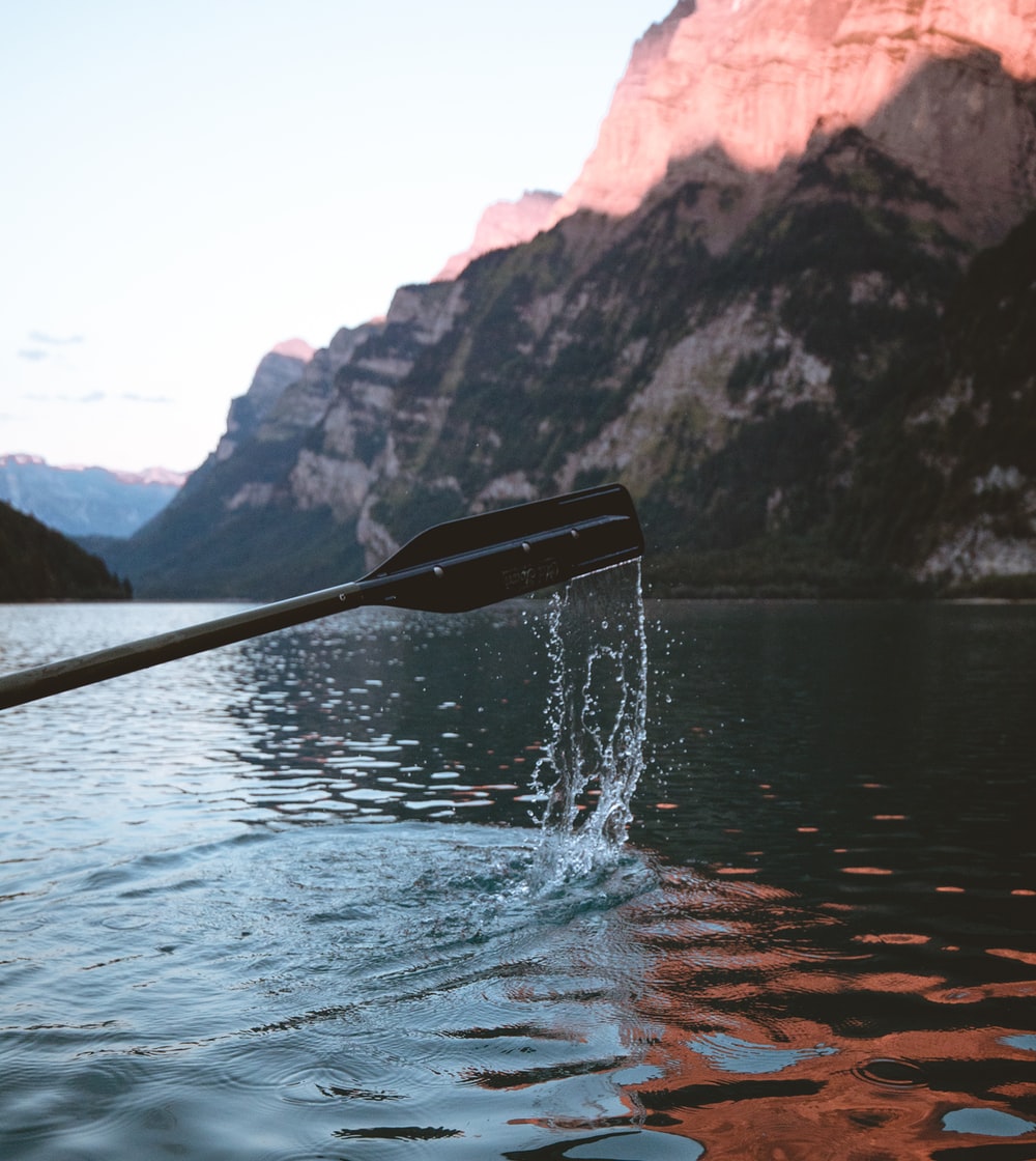 oar coming out of water, dripping water, in front of mountains