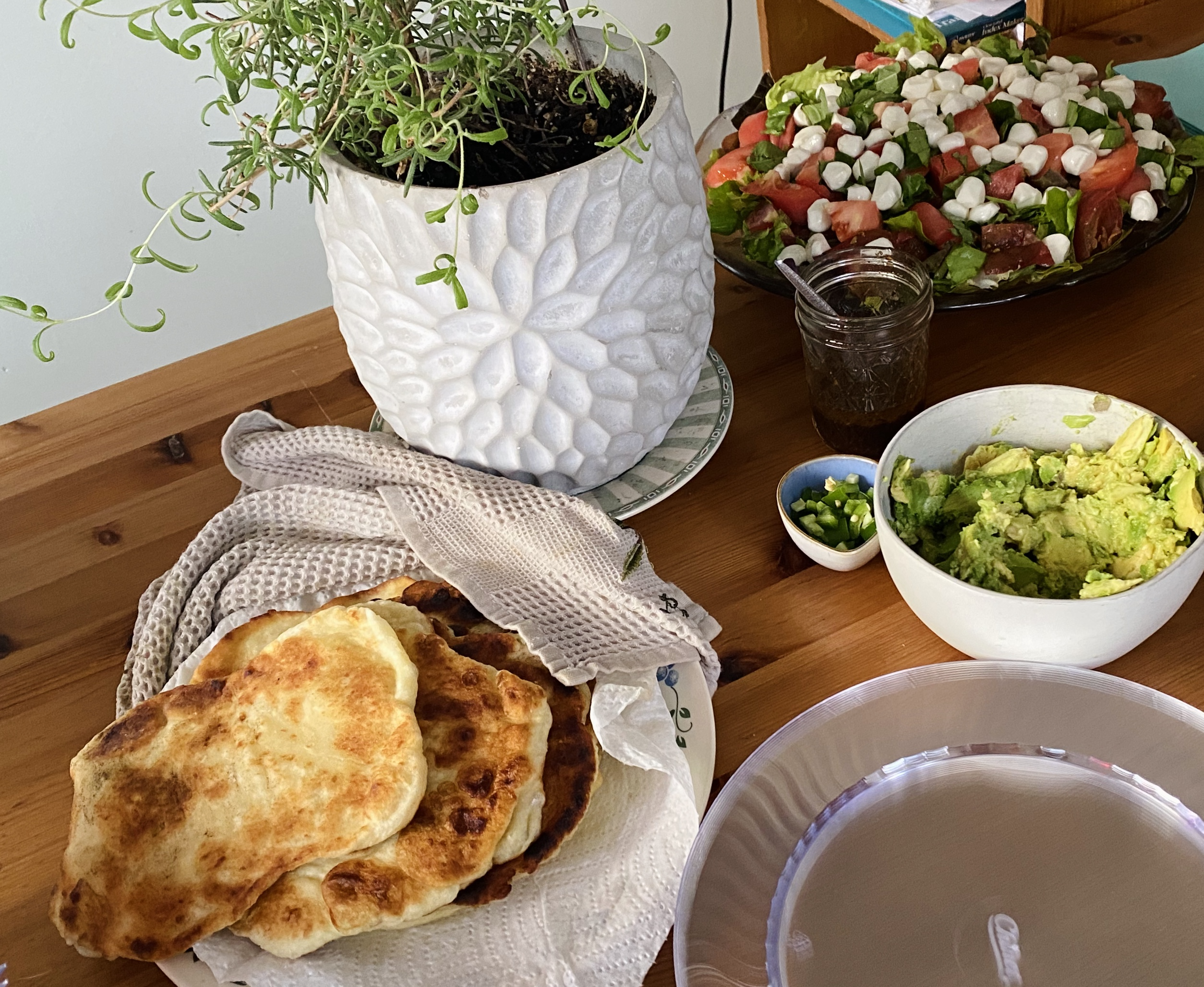 Pillowy flatbreads in a dish next to some smashed avocado and summer caprese salad