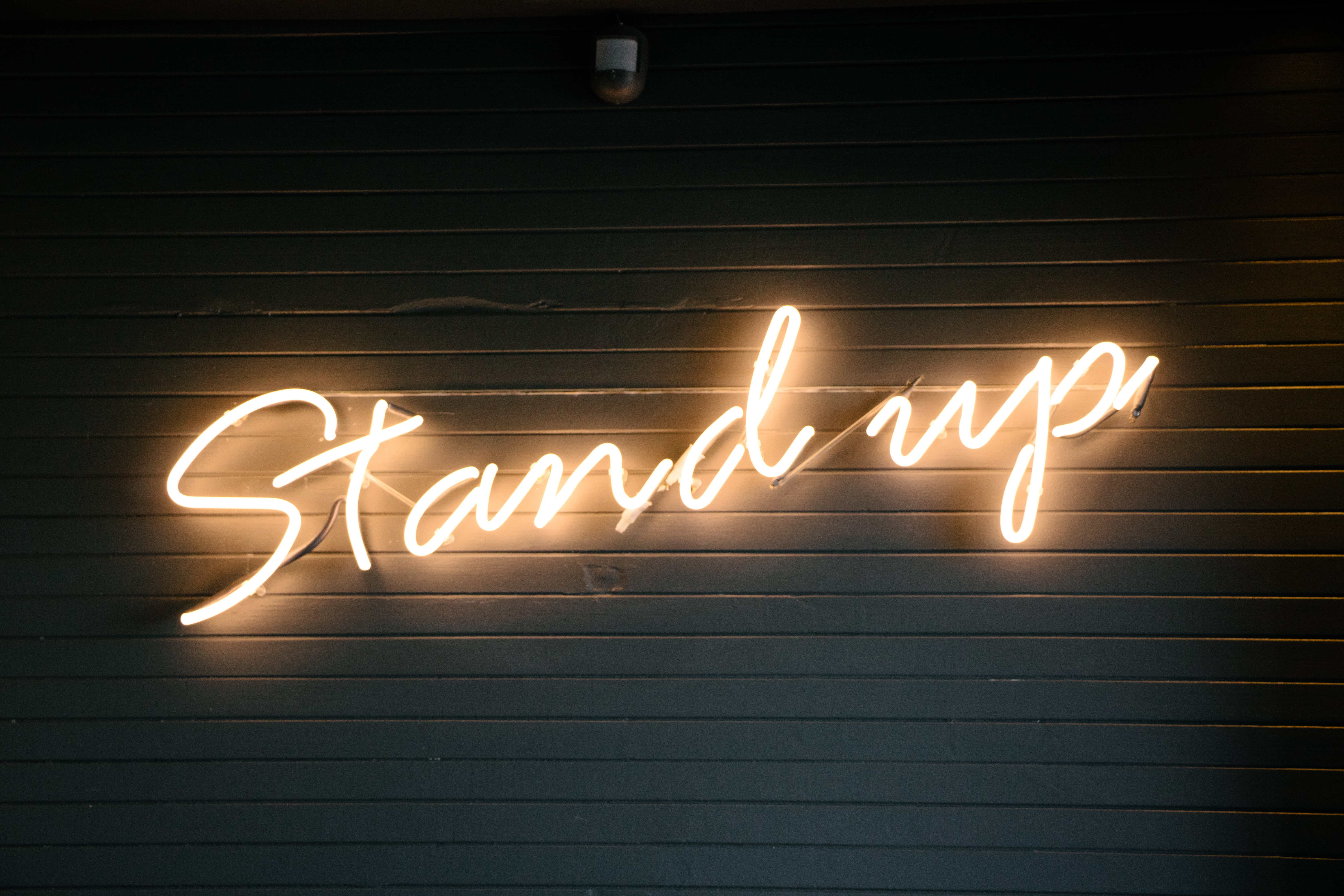 The phrase "Stand up" in a lighted sign on a slatted wooden backdrop