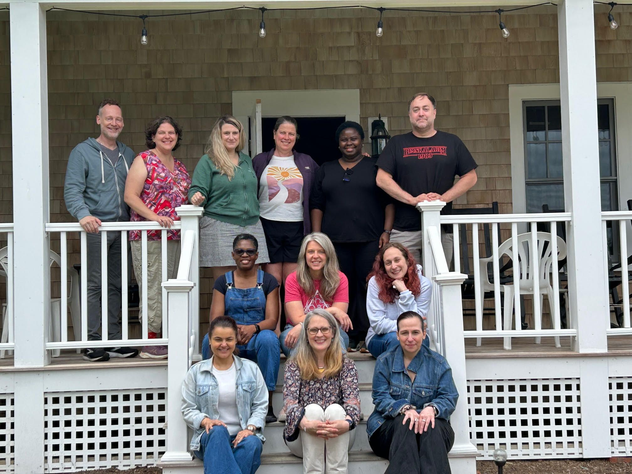 Twelve Simmons University employees smile in three rows on a beach house porch