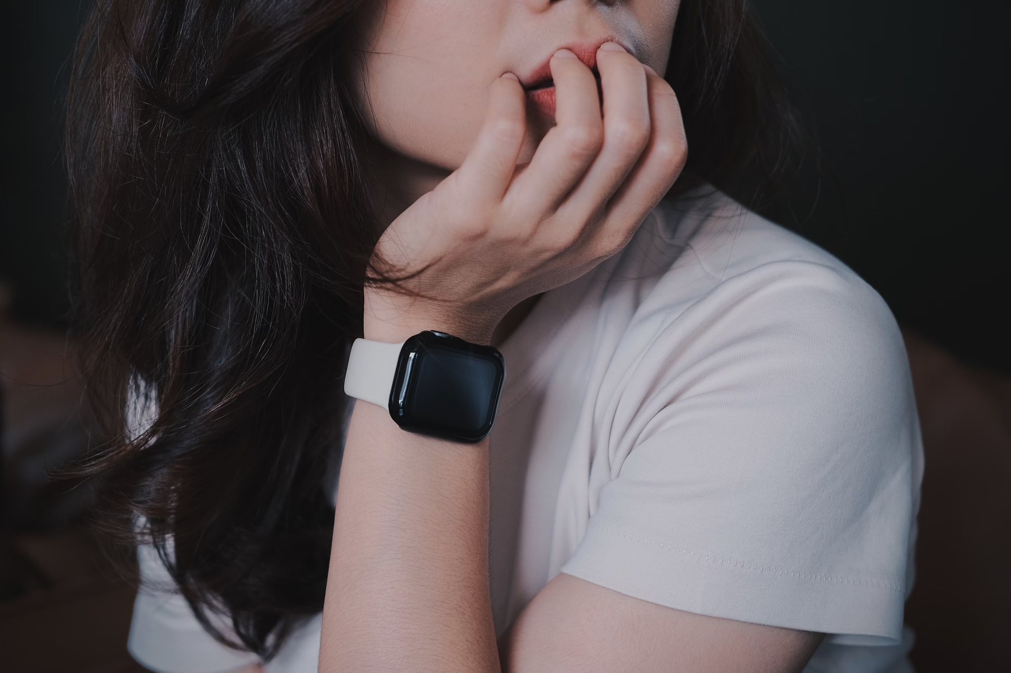 Woman with long black hair wearing a smart watch and looking pensive