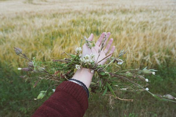 Hand outstretched with a flower crown on the wrist - background is a field adn she is wearing a red sweater
