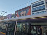 a luas car speeds by in full view. behind it are 4 non descript city buildings, with one more building in the middle that says "unite the union"- also has a mural of a black irish man