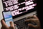 an obscured hacker types on a phone terminal while also using a laptop terminal console window