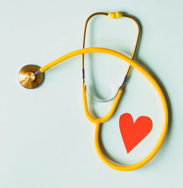 a yellow stethoscope on a cream background with a red paper heart inside its loop