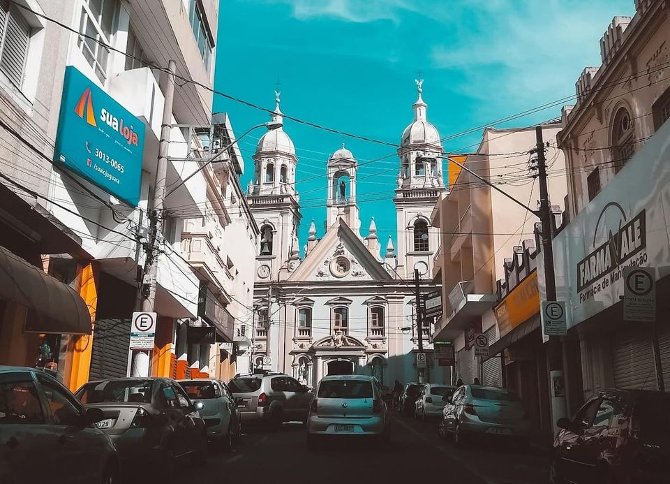 a brazilian street with cars, a white church, and mostly white buildings on either side of the church
