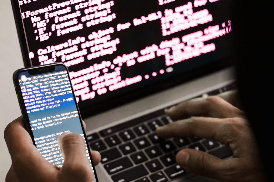 an obscured hacker types on a phone terminal while also using a laptop terminal console window