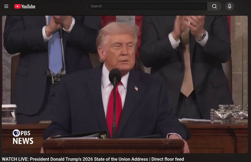 a photo of president trump standing in front of congress wearing a red tie. he is squinting and two men are clapping behind him