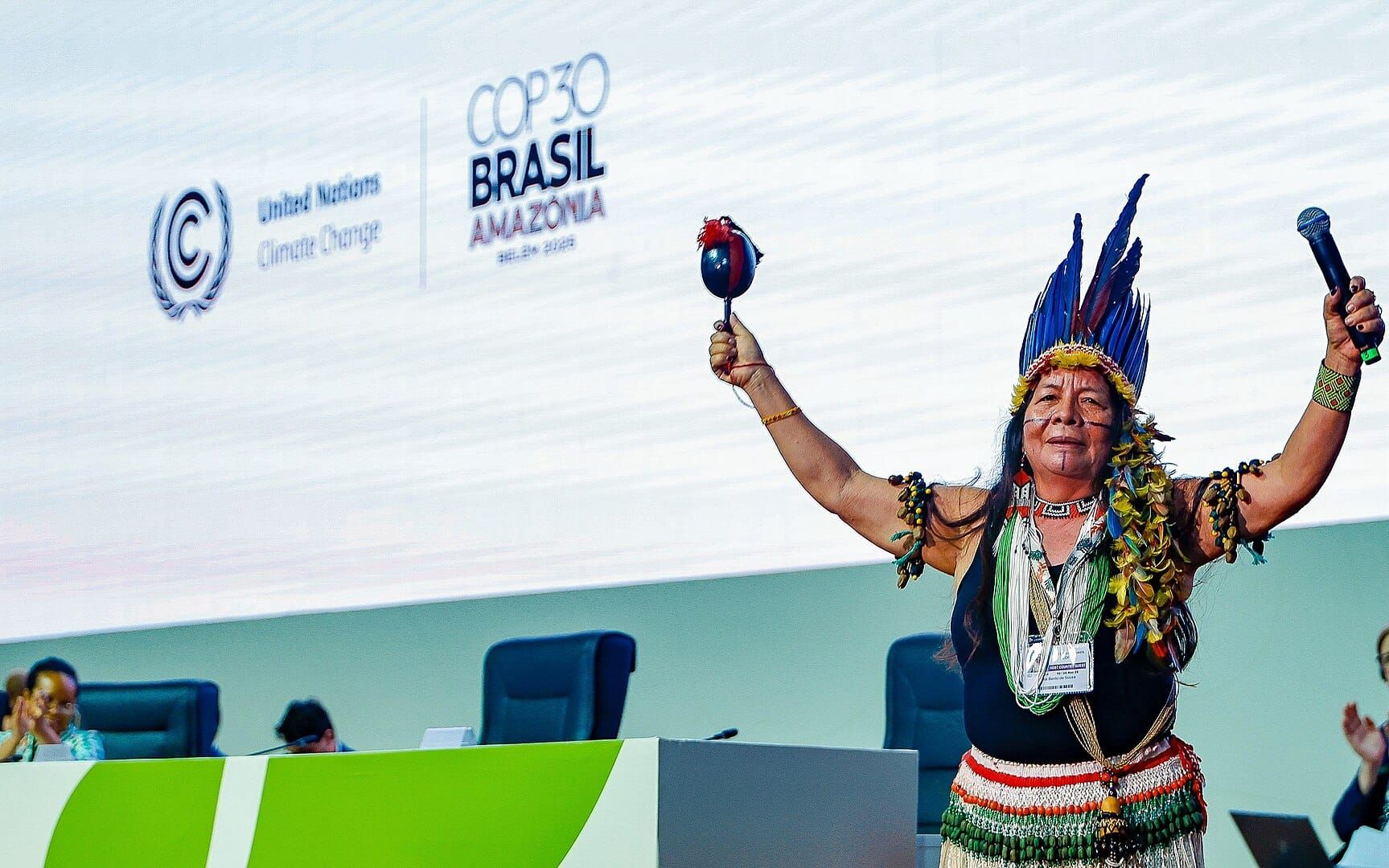Photo of an indigenous woman on a dais in front of a large screen, opening COP30.