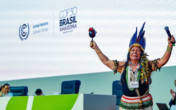 Photo of an indigenous woman on a dais in front of a large screen, opening COP30.