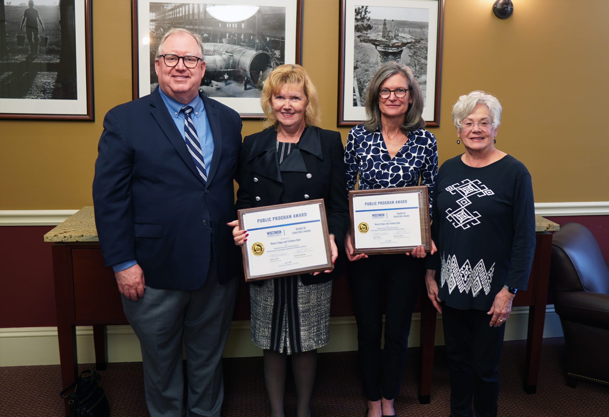 Nancy Kopp and Colleen Ball pose for a picture with two members of the Board of Curators while each holding a plaque that says Public Program Award