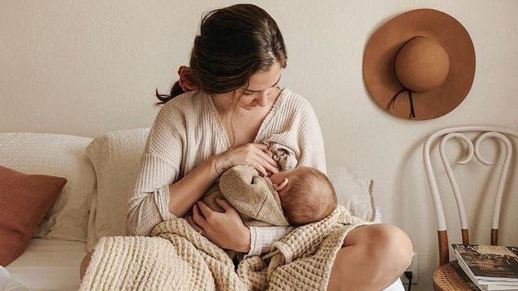Mère allaitant son bébé dans un moment de calme sur un lit, favorisant le lien d’attachement et la lactation dans un environnement apaisant