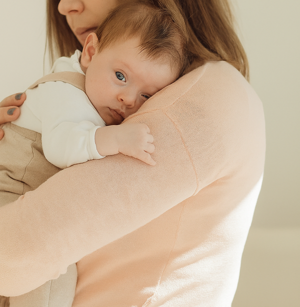 Maman tenant son bébé contre son épaule, main douce sur son dos, dans une ambiance lumineuse et apaisante.">