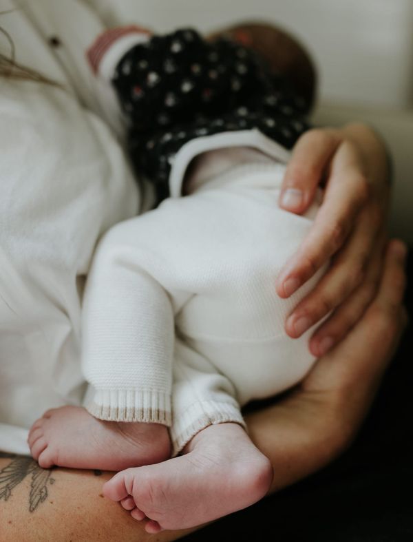 Bébé en pyjama blanc blotti contre un adulte pendant une tétée, en position d'allaitement, capturant un moment de douceur et de proximité