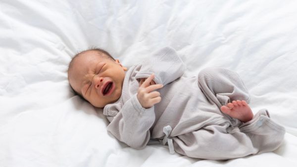 Nourrisson allongé sur un lit, pleurant et exprimant une gêne, illustrant les situations d’inconfort ou de détresse qui peuvent inquiéter les jeunes parents.