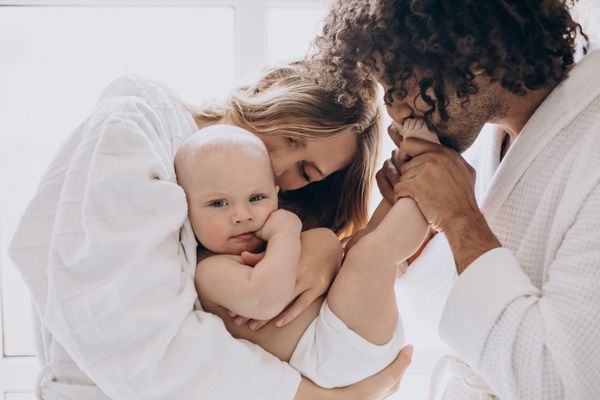 eunes parents câlinant leur bébé dans un moment tendre à la maison, illustrant le lien parent-bébé et la douceur du quotidien familial.