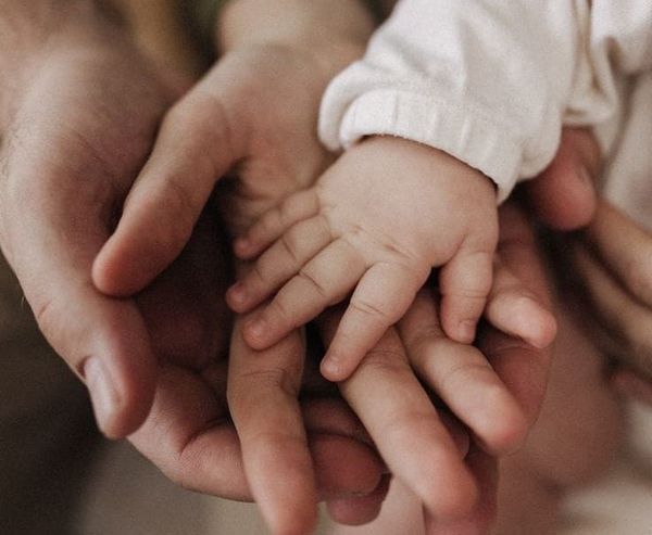 Main d’un parent tenant délicatement la main de son nouveau-né, symbole de lien d’attachement, de sécurité et de proximité parent-bébé.