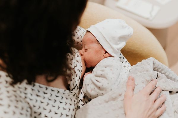 Maman allaitant son nouveau-né confortablement installé dans ses bras, moment de peau à peau favorisant le lien et un allaitement serein.