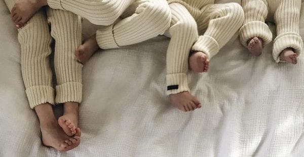 Jambes et pieds de trois enfants allongés sur un lit, portant des tenues assorties en maille beige, symbole de fratrie et vie de famille.
