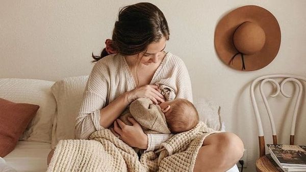 Mère allaitant son bébé dans un moment de calme sur un lit, favorisant le lien d’attachement et la lactation dans un environnement apaisant
