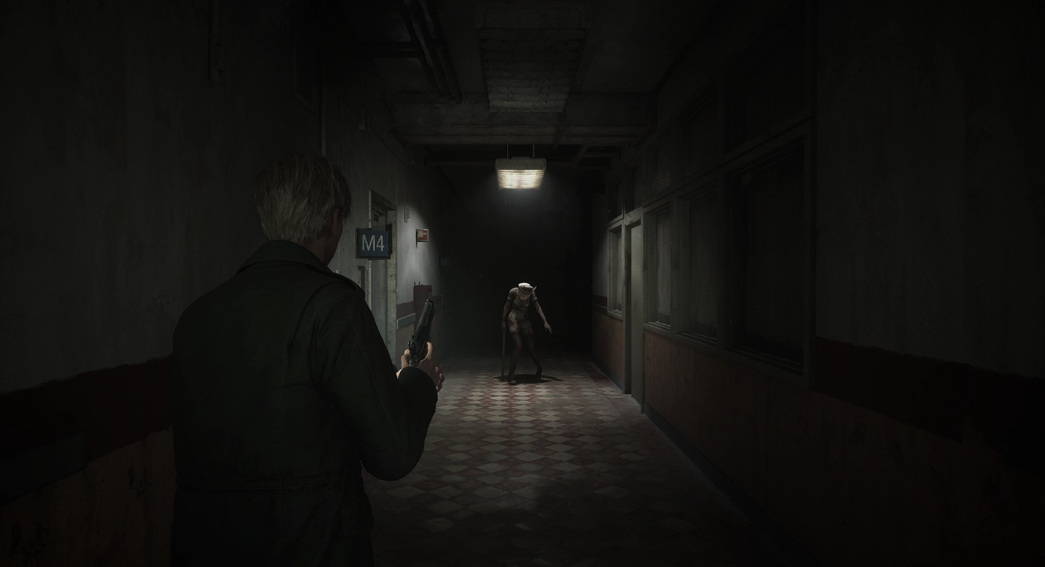 Silent Hill 2 protagonist James Sunderland faces down a dark corridor, where a nurse monster under a spotlight staggers towards him