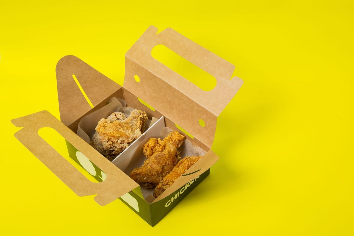 Delicious crispy fried chicken served in an open cardboard box on a vibrant yellow background.