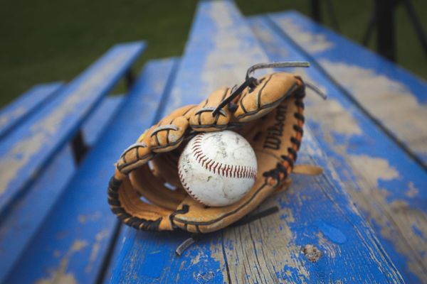 A white baseball in a leather baseball glove, on a blue bleacher
