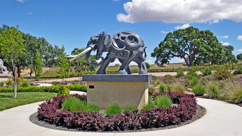 A stone elephant standing on a platform, surrounded by a pathway and plants. 
