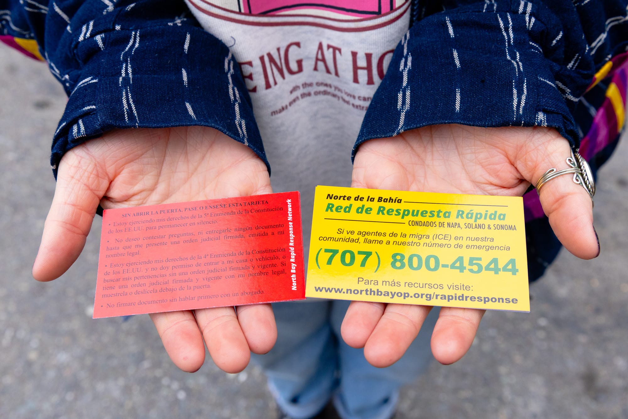 two hands display red and yellow cards with instructions in Spanish about what to do in ICE interactions