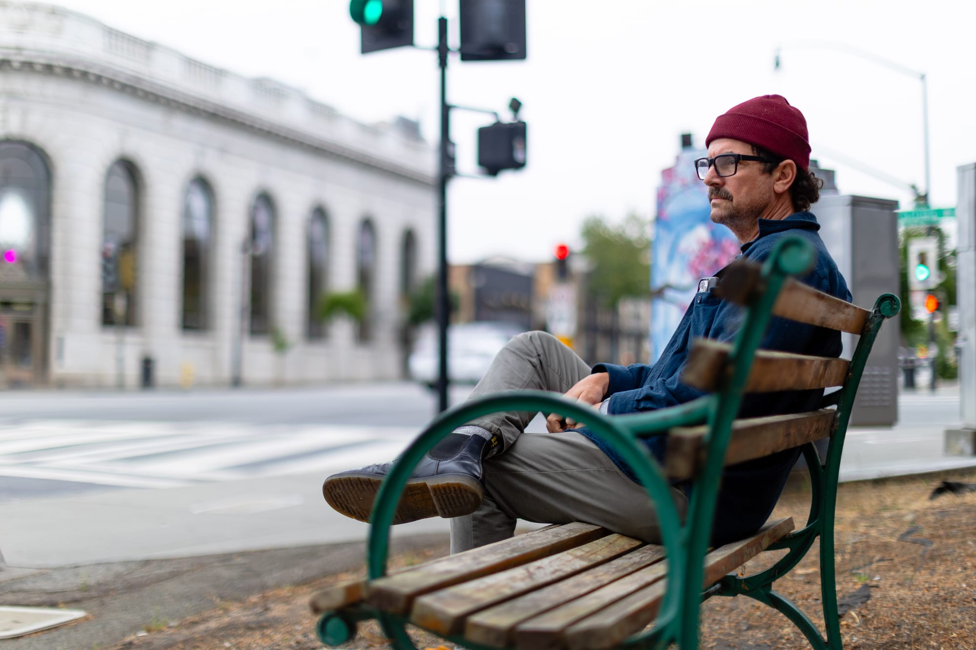 a white man with black rimed glasses sits on a bench