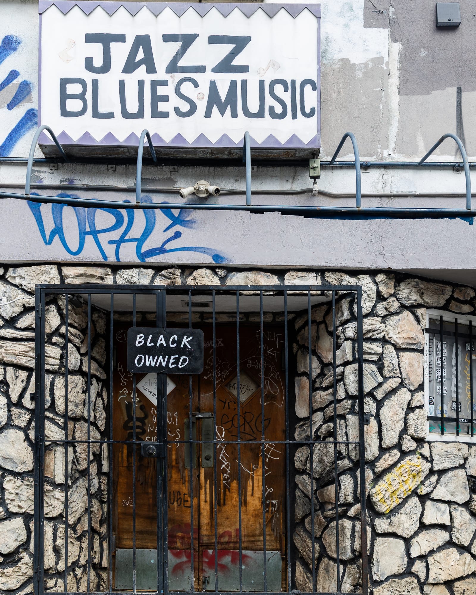 The facade of Esther's Orbit Room. A sign above the gated entry says "Blues Music," while a smaller sign on the gate says "Black Owned"