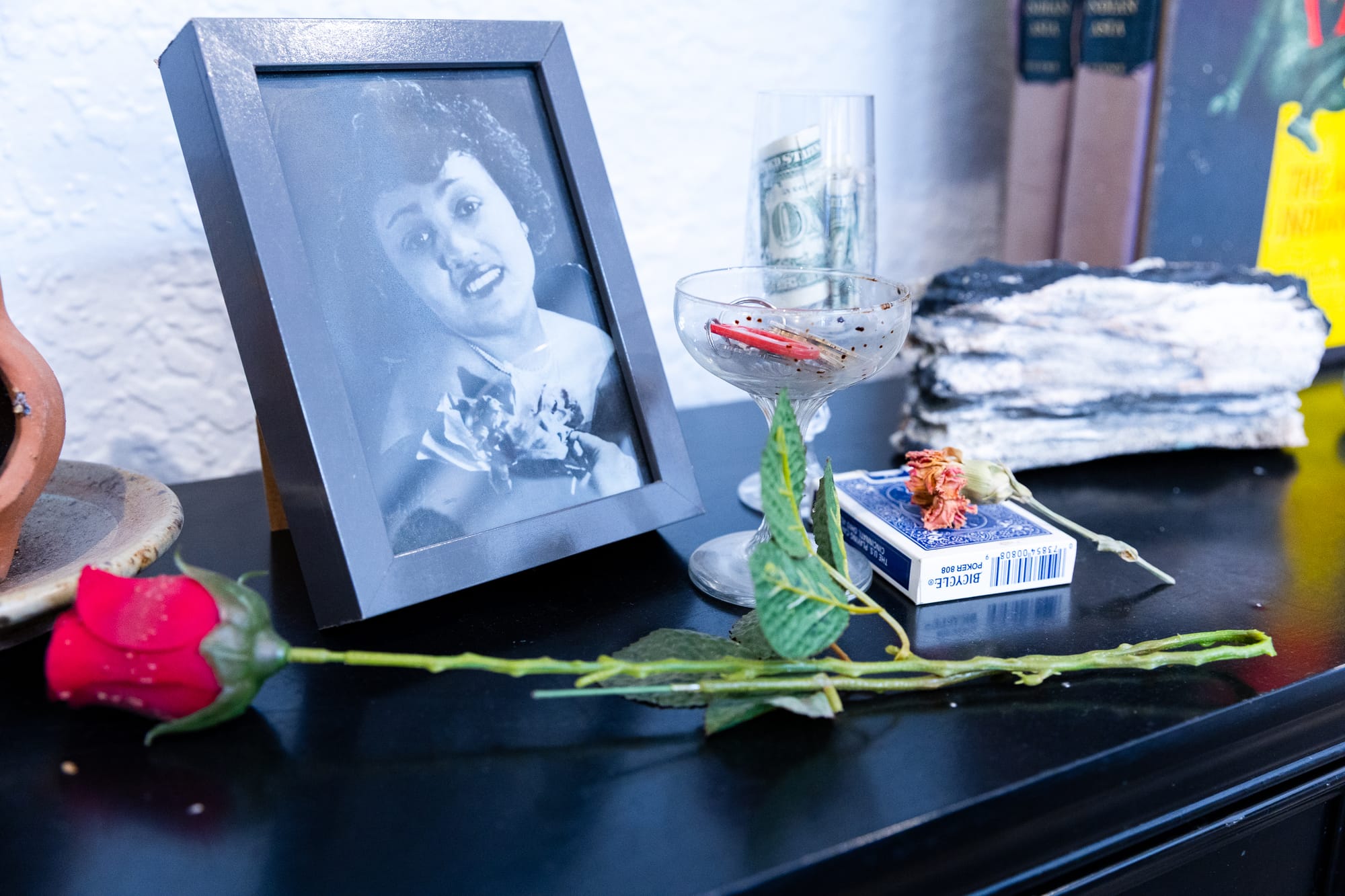 A modest altar includes a framed photo of Esther Mabry, a plastic rose, glasses containing keys and cash, and a package of playing cards.