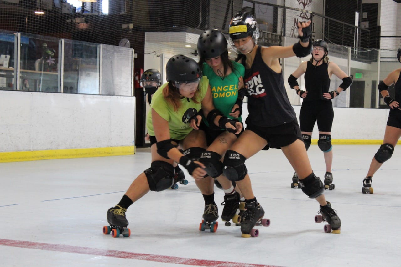 A person in a forest green t-shirt trying to push through two other skaters who are trying to keep them out