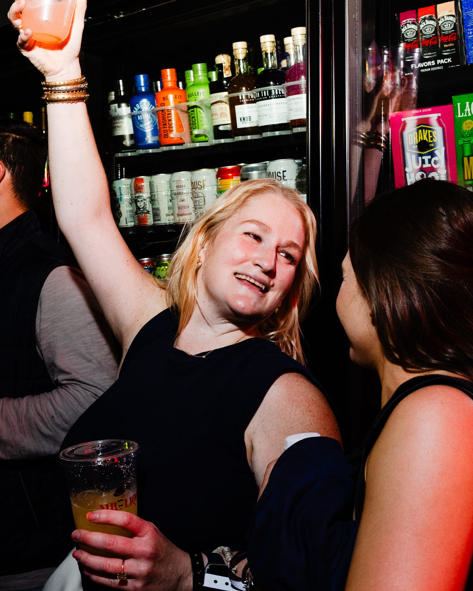 A person holding two drinks speaks with their friend. 