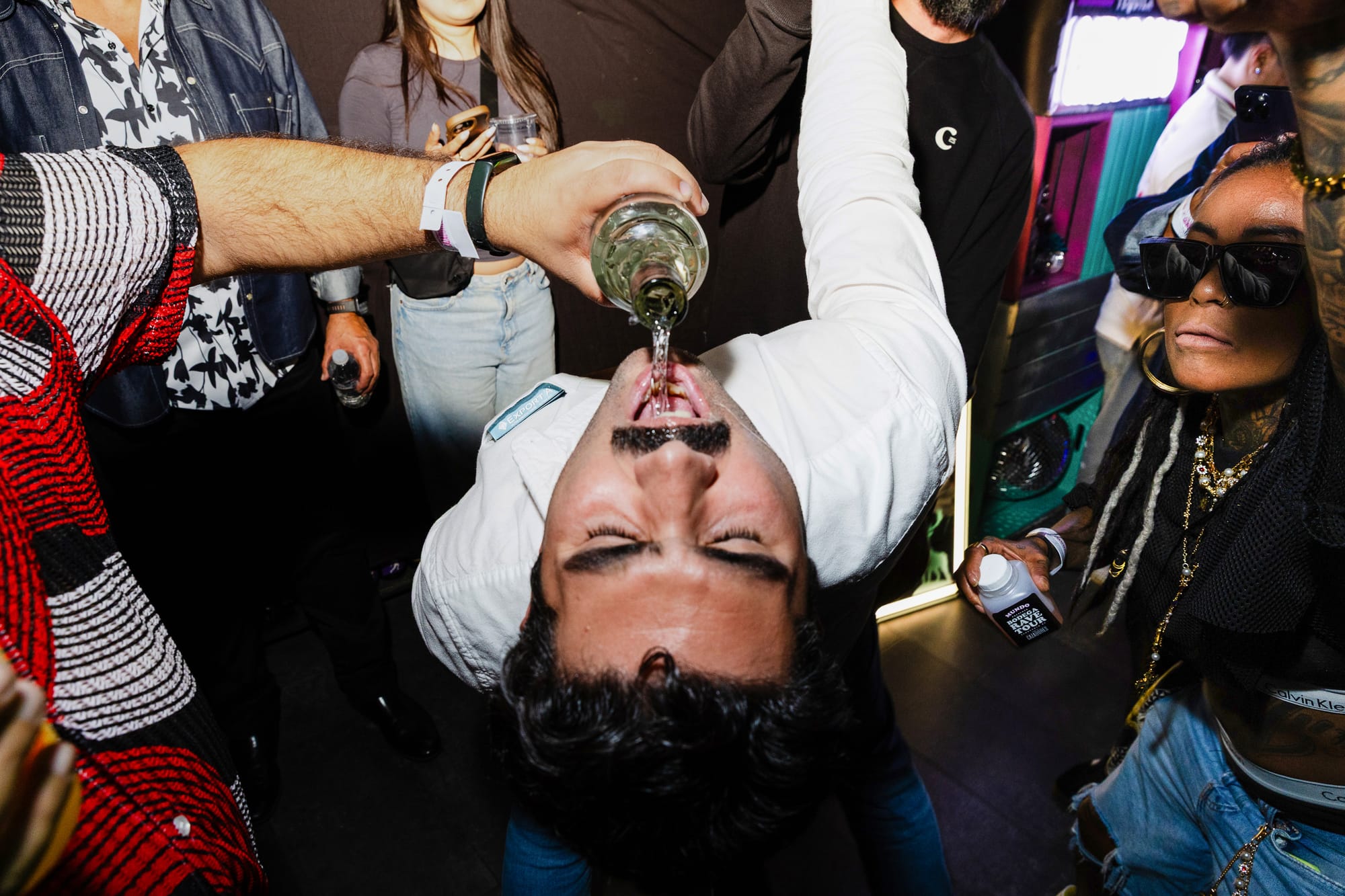 A person pours tequila into the mouth of another person doing a backbend as people in the background cheer. 