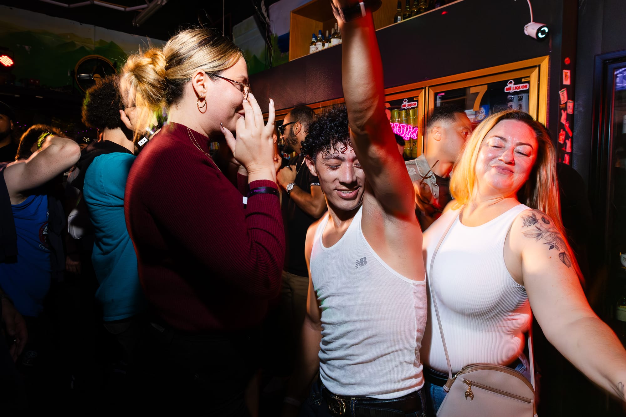 Three people dance closely in a cowed room. The one in the center has their arm up in the air. 