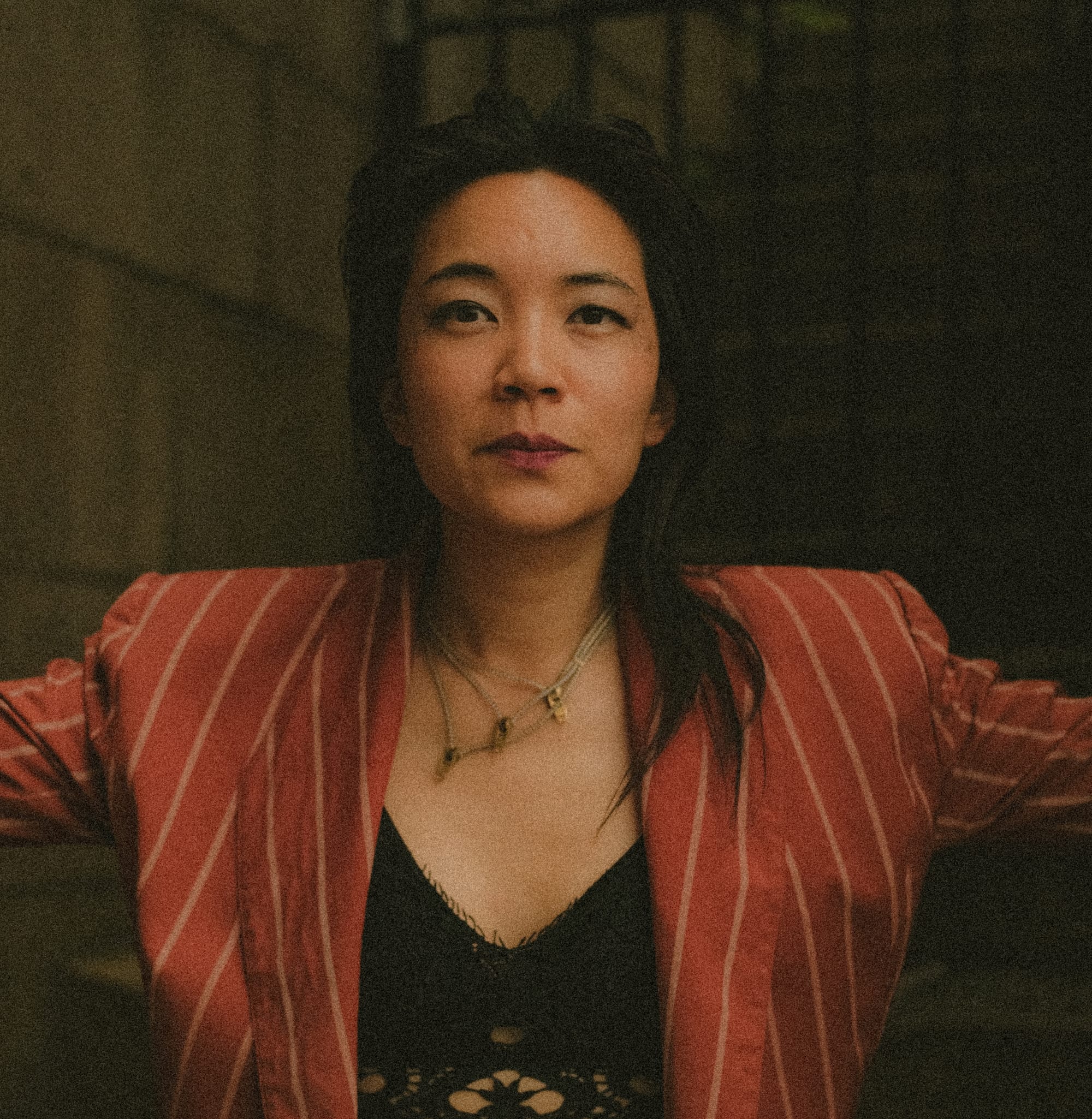 a Vietnamese American woman, musician Thao Nguyen, wears a black lace top and red striped blazer and looks into the camera for a potrait