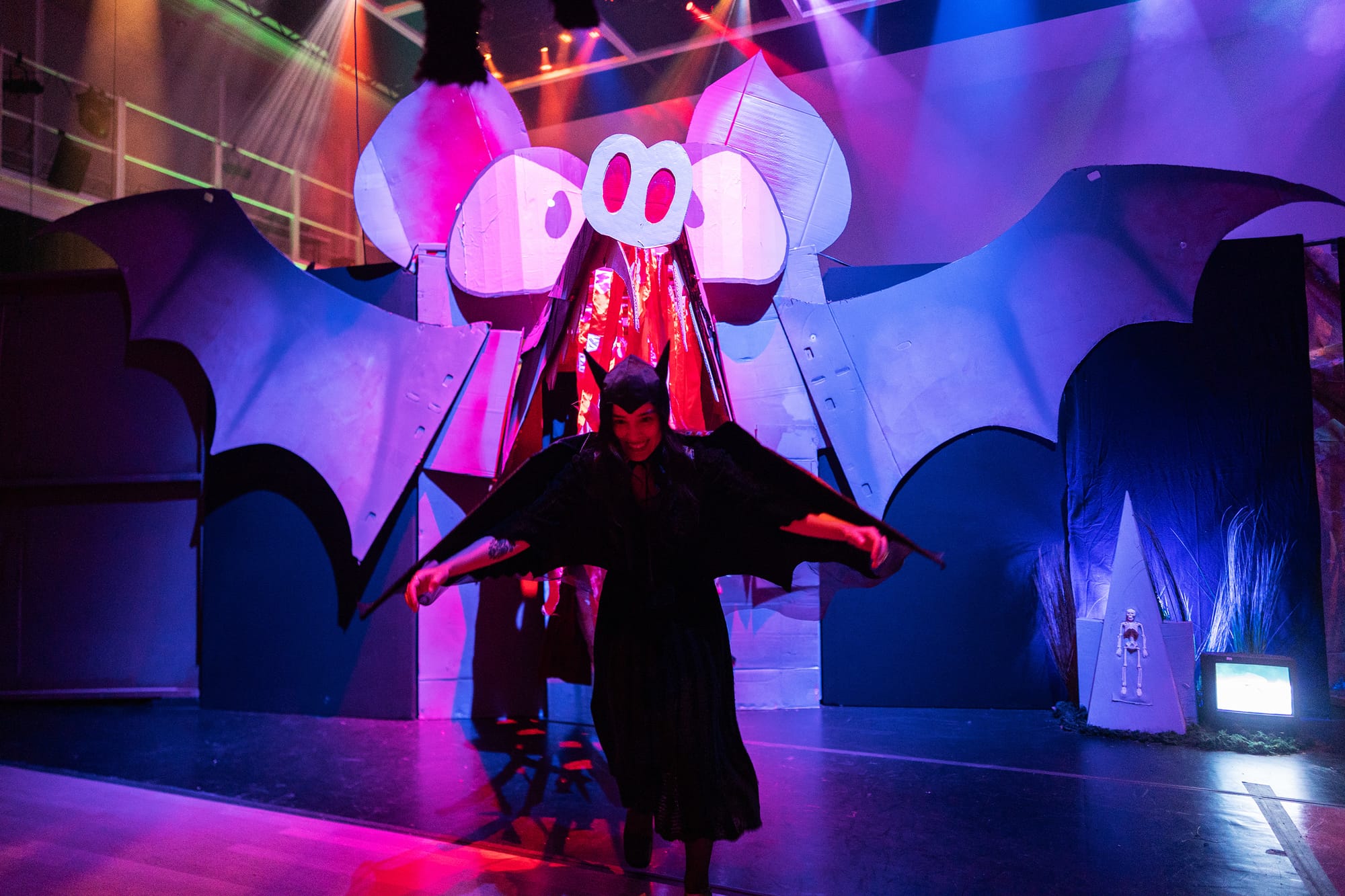 Person in bat costume posing in front of giant cardboard cartoon bat.