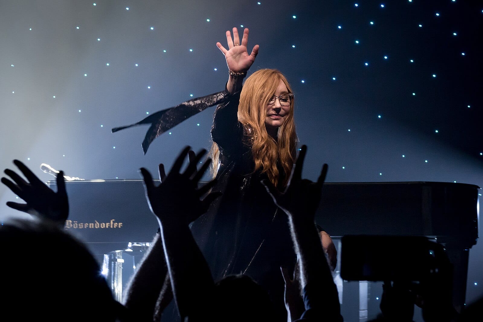 Tori Amos waves at cheering fans in the crowd as she performs.