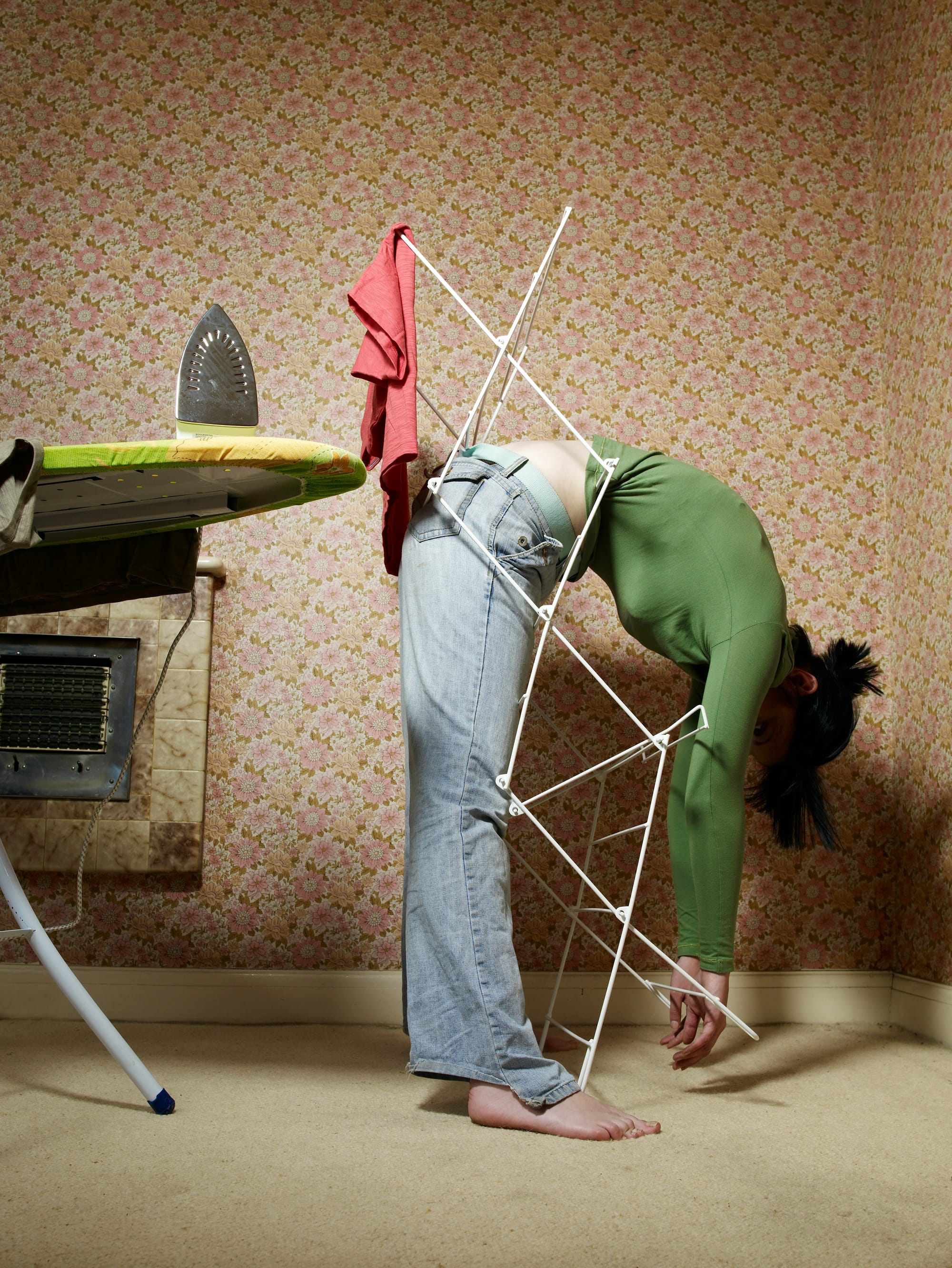 a woman in a green shirt and jeans is draped over a laundry rack for some reason