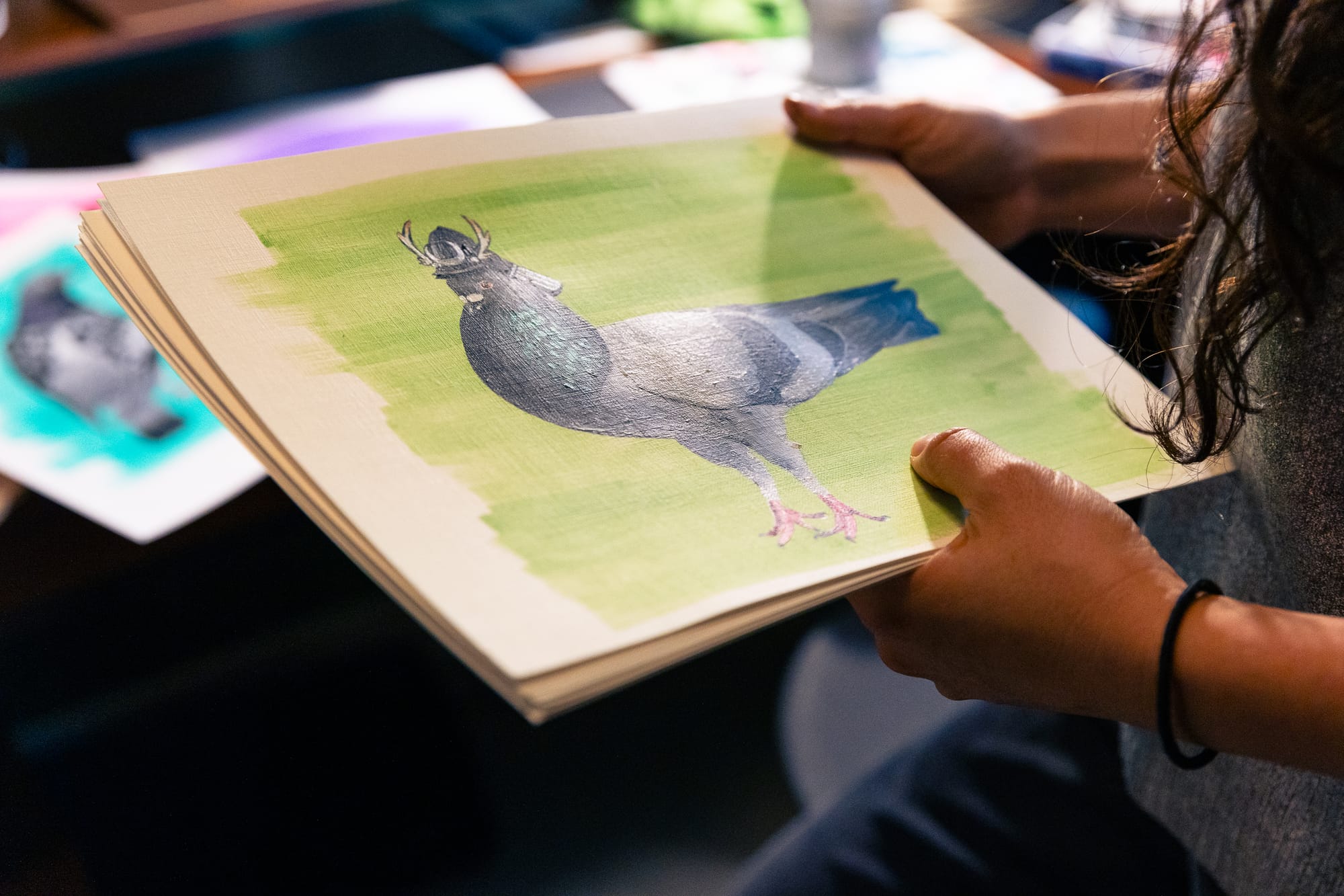 A person holding a painting of a pigeon, in which the pigeon is wearing an old style military helmet