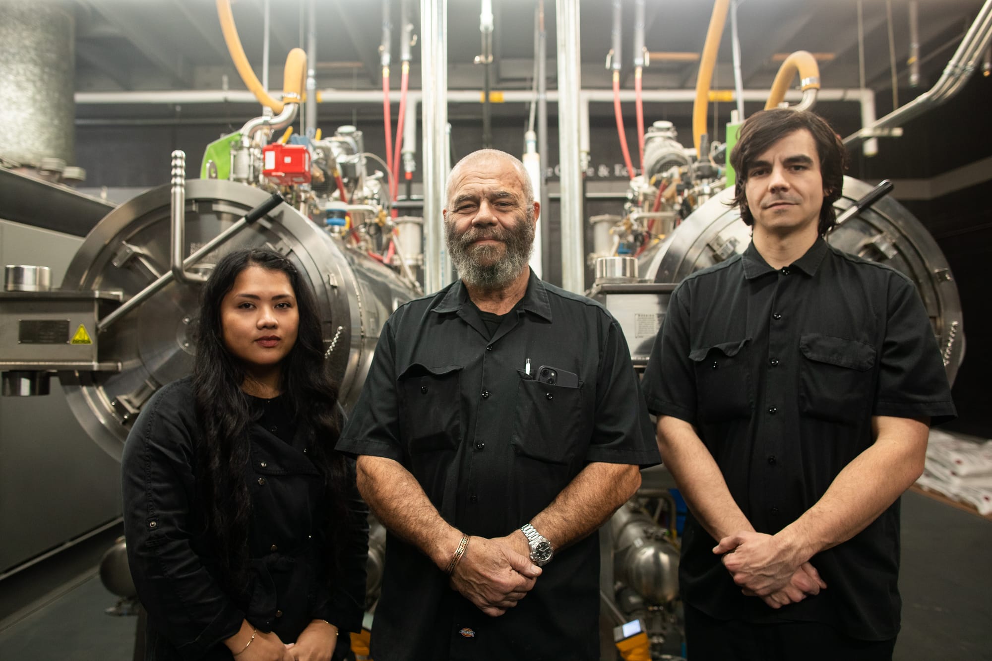 Three people dressed in black standing in front of aquamation machinery.